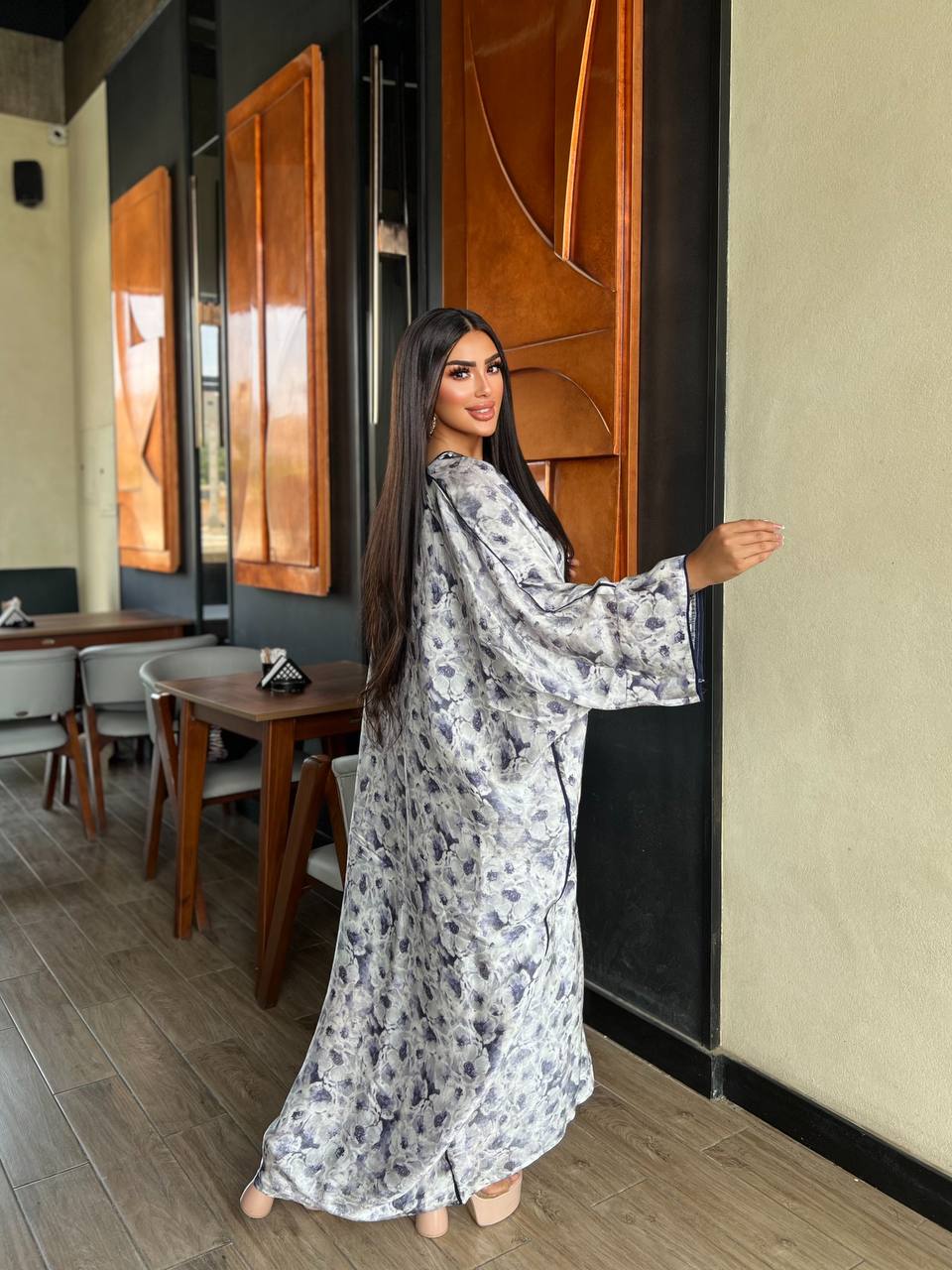 Woman in a floral dress standing in a modern interior setting with wooden furniture.
